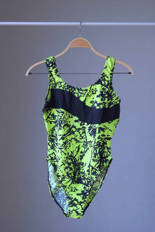 Front view of a vintage Danskin leotard in neon lime green and black, hanging on a clothes rack.