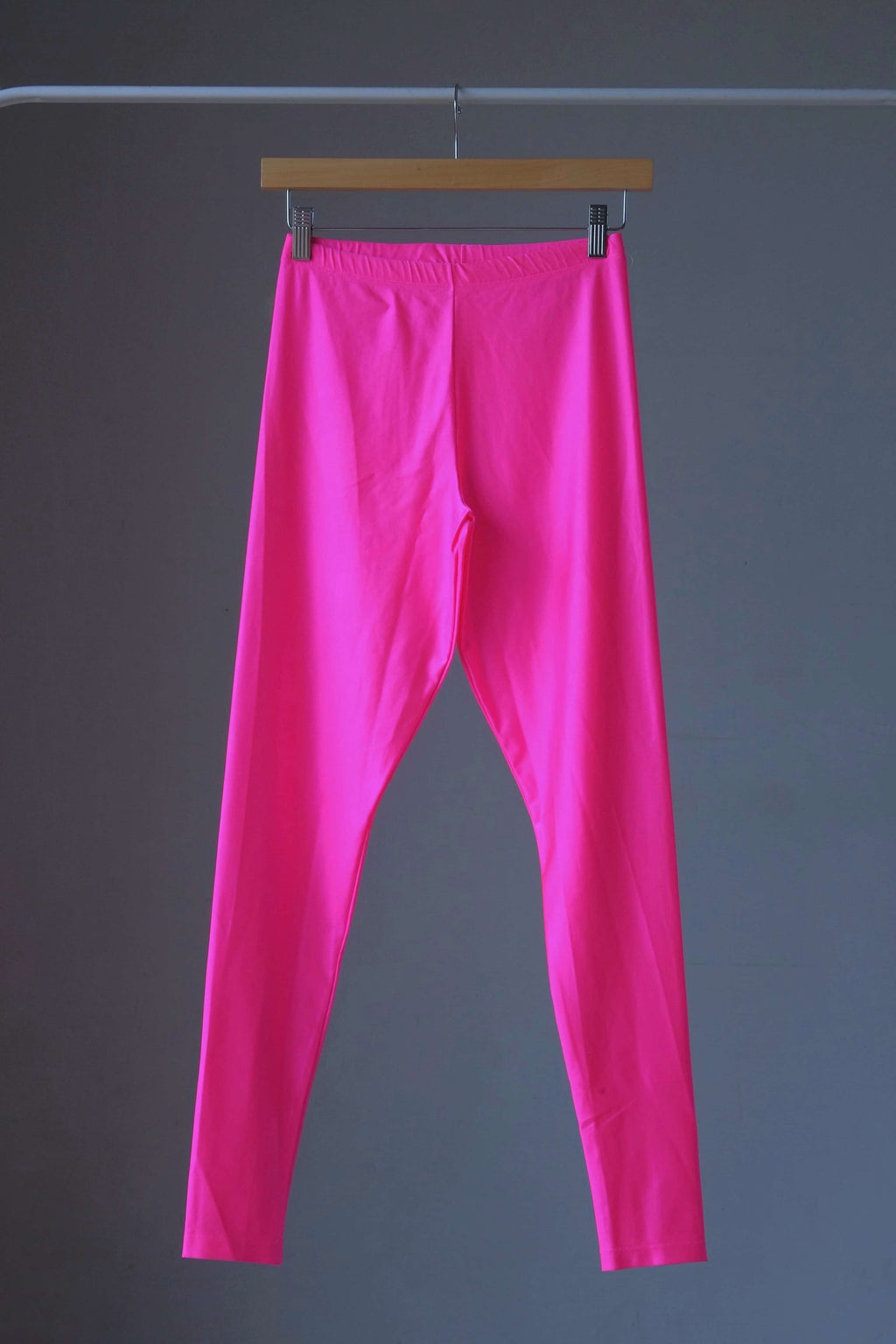 A pair of shiny neon pink vintage 90s Danskin high-waist leggings displayed on a hanger.