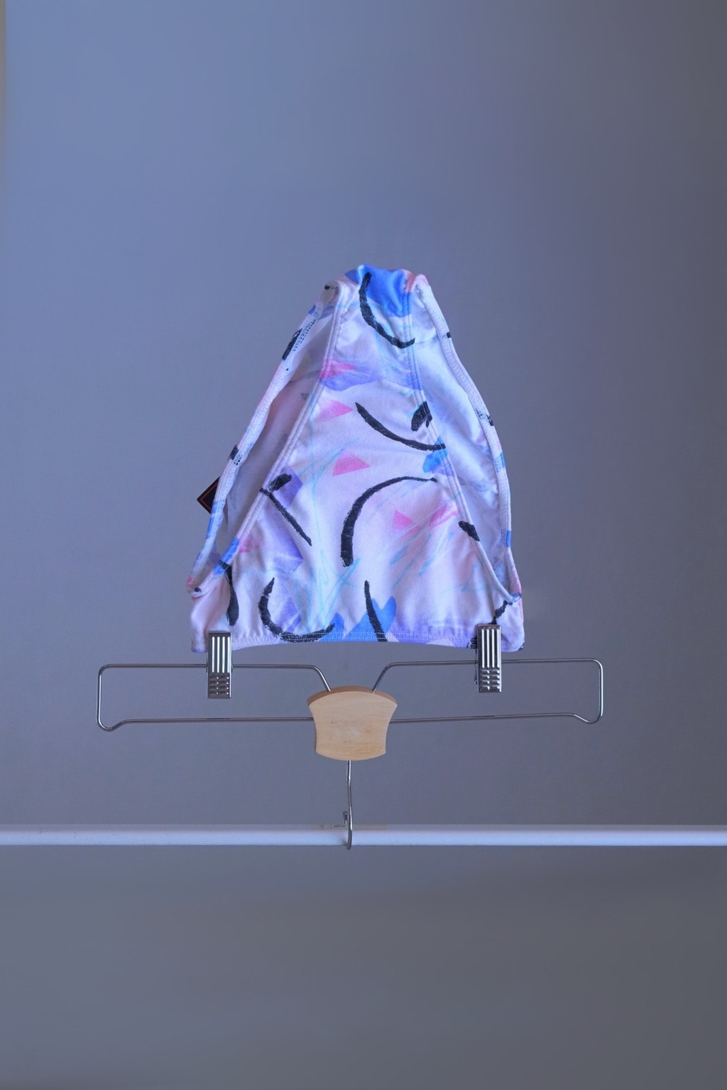 A pair of vintage 90s DANSKIN dance briefs with a white base and blue, purple, and black pastel print, displayed on a hanger.