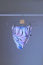 A pair of vintage 90s DANSKIN dance briefs with a white base and blue, purple, and black pastel print, displayed on a hanger.