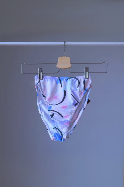 A DANSKIN vintage 90s high-cut activewear brief with an abstract pastel print, displayed on a hanger.