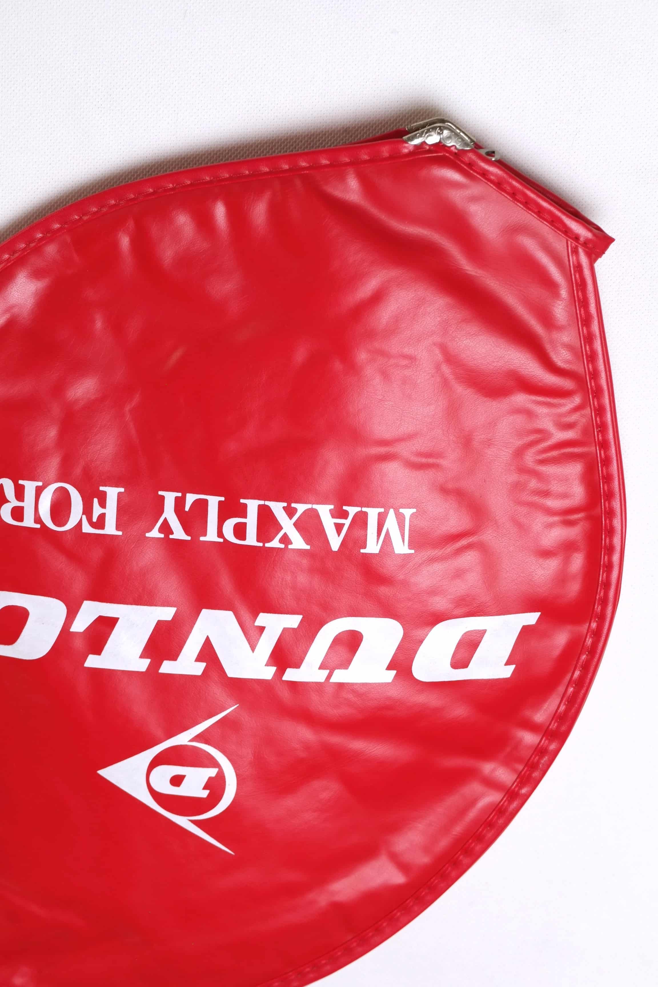 Close-up shot of the white printed Dunlop Maxply Fort logo on a vibrant red textured vinyl vintage tennis racket cover.