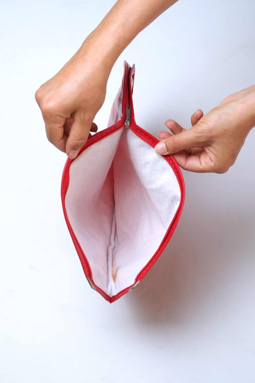 Two hands holding open a vintage red vinyl Dunlop tennis racket head cover, showing the soft white protective fleece lining and a silver metal zipper pull.