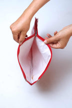 Two hands holding open a vintage red vinyl Dunlop tennis racket head cover, showing the soft white protective fleece lining and a silver metal zipper pull.