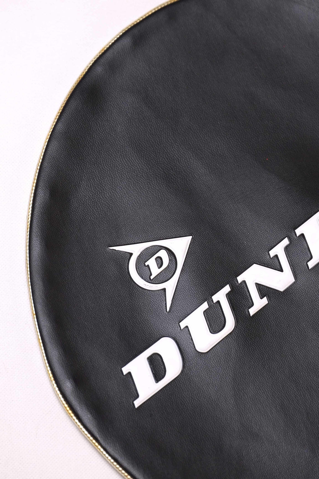 Detailed shot of the white embossed Dunlop logo and lettering on a black grained vinyl vintage tennis racket cover.