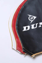 Close-up view of stacked vintage vinyl Dunlop tennis racket covers in black, red, and white, highlighting the stitched edges and gold-tone zippers.