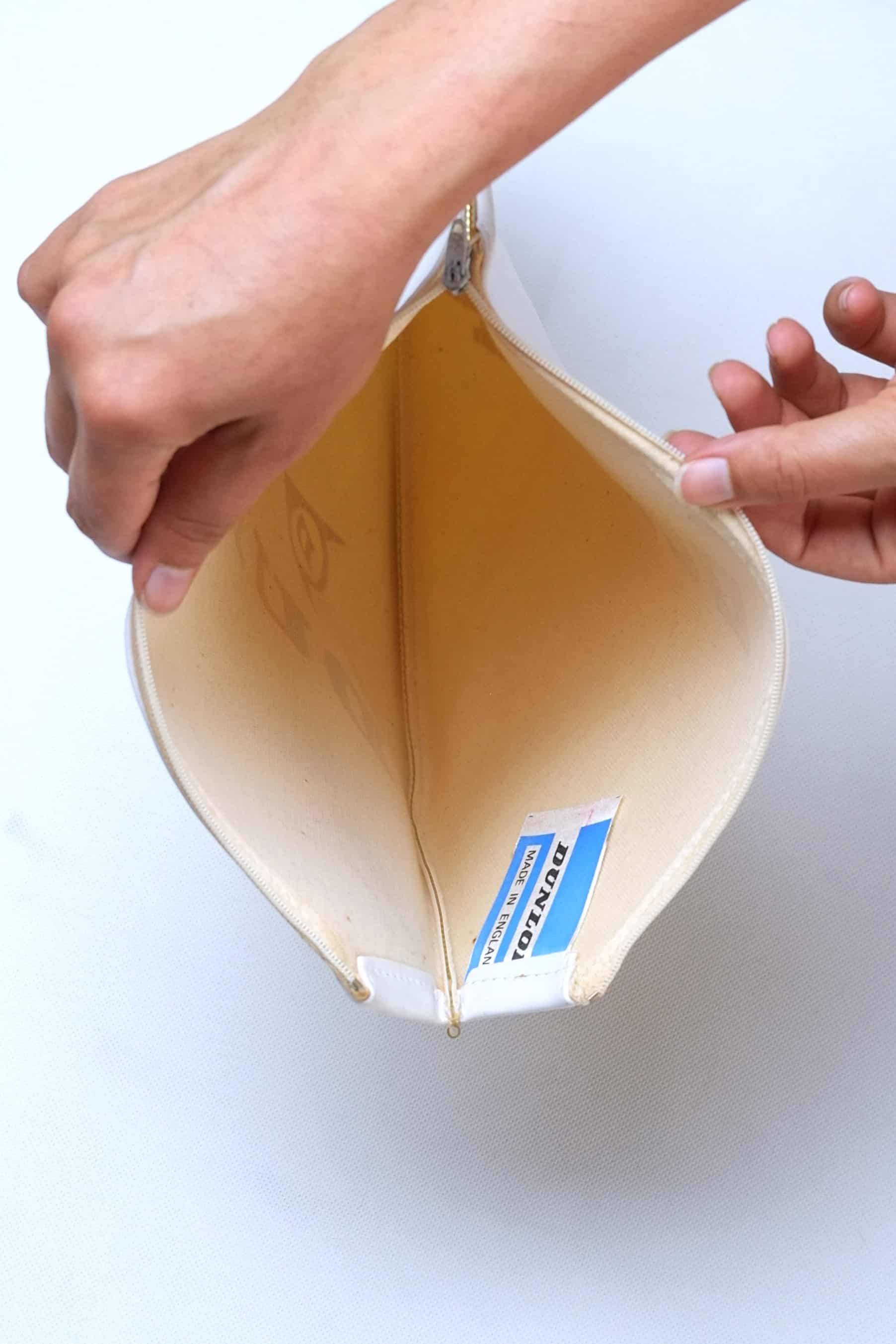 Two hands opening a vintage white vinyl Dunlop tennis racket cover to display the clean cloth interior lining and authentic Made in England tag.