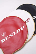 Overhead tight shot of three vintage Dunlop vinyl tennis racket head covers fanned out in red, white, and black with embossed white branding.