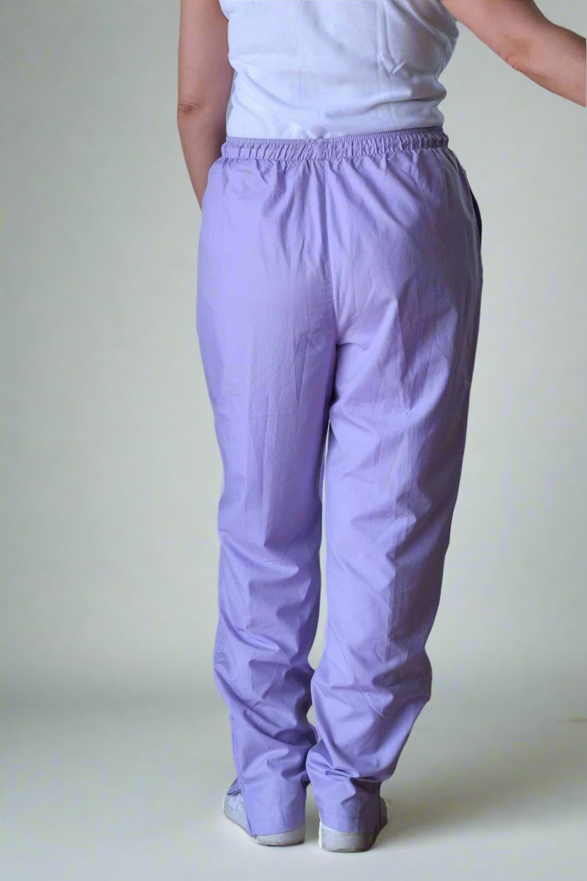 Back shot of Person wearing vintage Ellesse lilac track pants with an elastic waistband and relaxed fit, paired with a sleeveless white polo shirt and white sneakers, standing indoors against a neutral background.