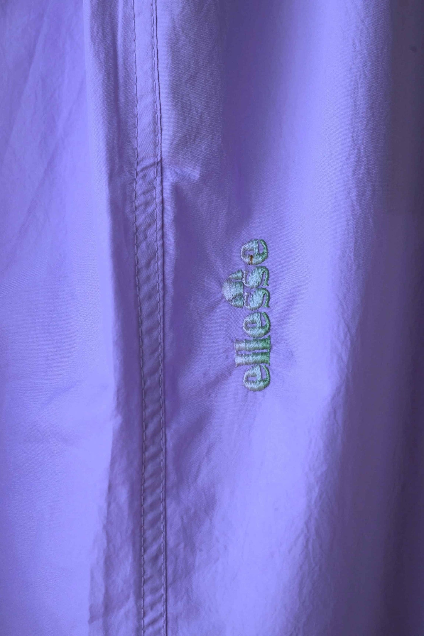 A close-up of the Ellesse brand logo on lilac-colored vintage track pants.