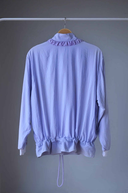 Vintage Ellesse jacket in pastel purple with a drawstring hem, seen from the back and hanging on a hanger.