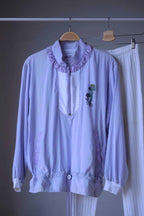 Close up of a Vintage Ellesse tracksuit in pastel purple and white, consisting of a cropped windbreaker with floral print and ribbed white leggings, hanging on a hanger with metal clips.