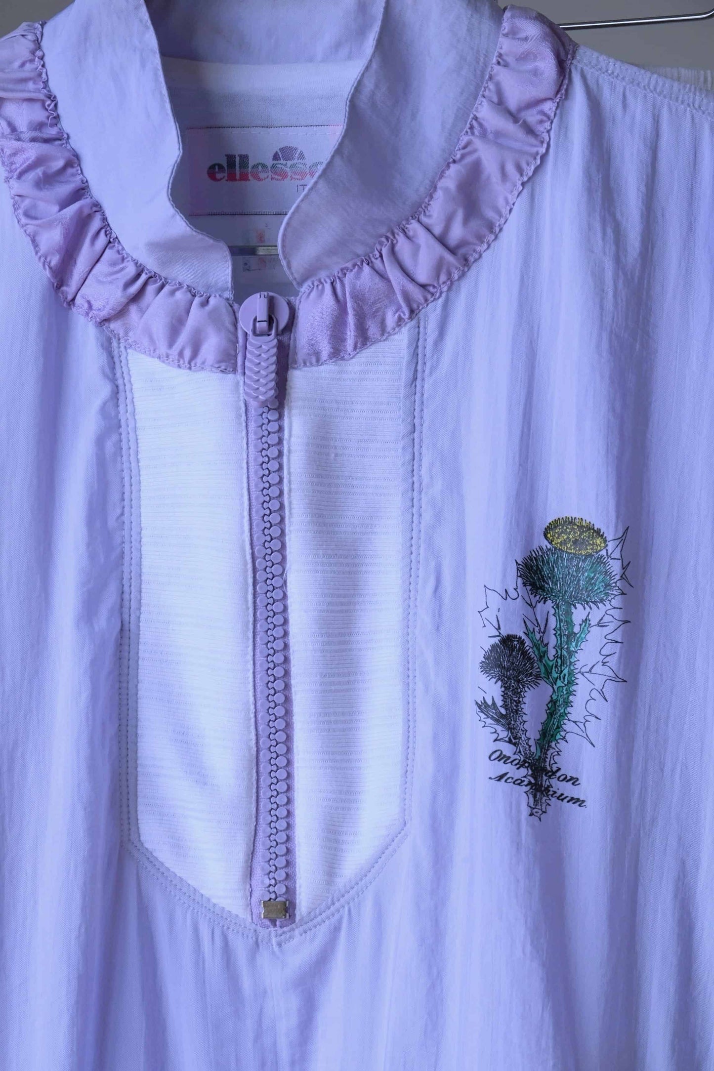 Detail of the Ellesse brand logo and floral print on a pastel purple Vintage Ellesse jacket.