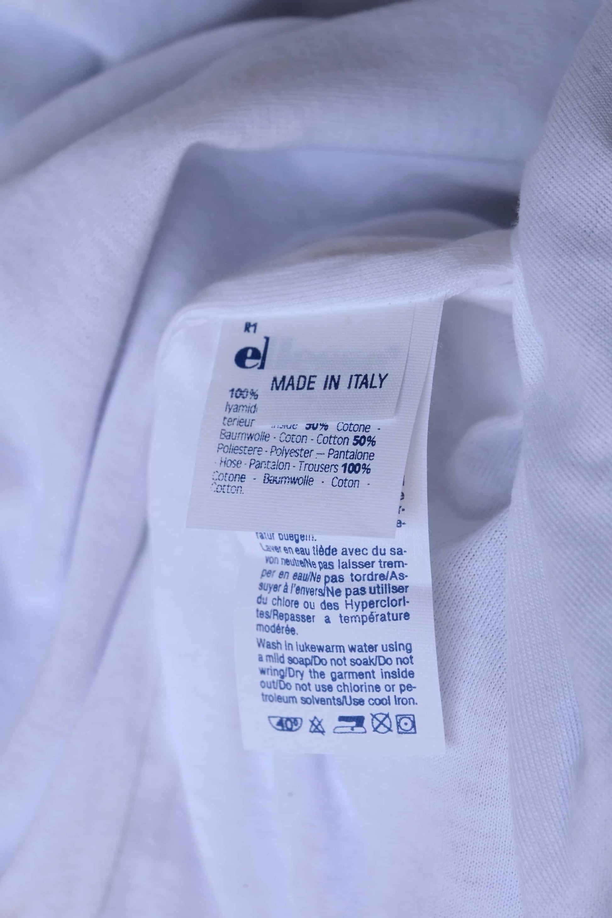 A close-up of a white clothing label with the text 'Made in Italy,' care instructions in multiple languages, and fabric content details.