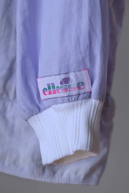 Detail of the Ellesse brand logo on a pastel purple jacket sleeve. The cuff is white and ribbed.