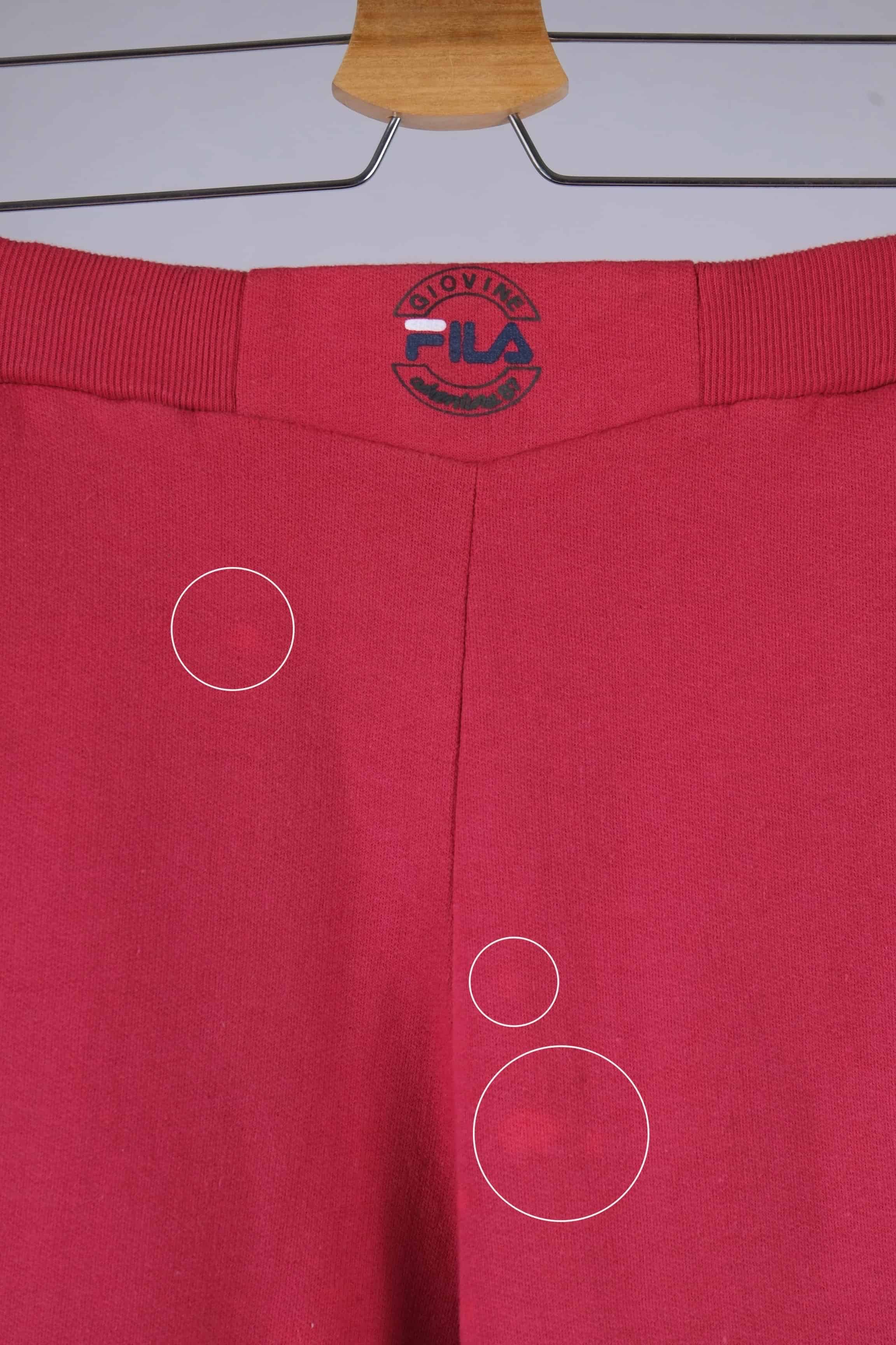 Close-up of the waistband of red Fila 90s vintage jogging pants, featuring the Fila logo in black, red, and blue.