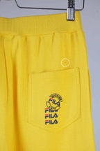 Close-up of the back pocket of yellow Fila 90s vintage jogging pants, showing the Fila logo in black, red, and blue.