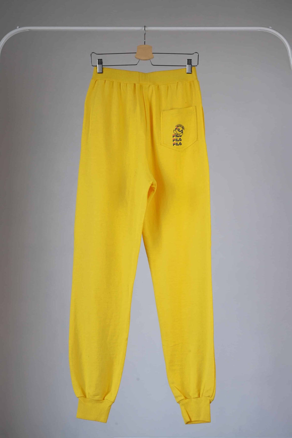 Back view of Yellow Fila 90s vintage jogging pants hanging on a hanger.