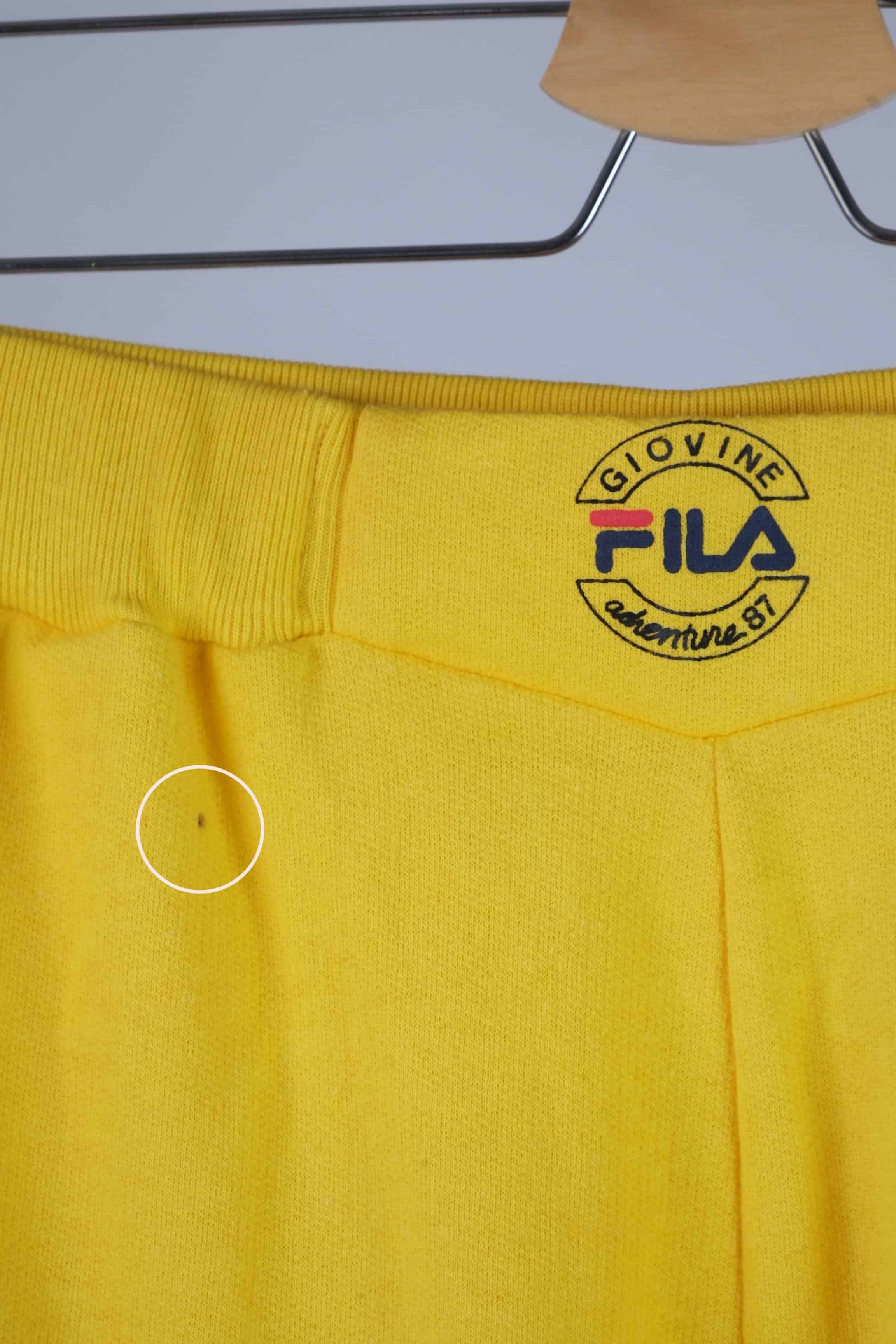 Close-up of the waistband of yellow Fila 90s vintage jogging pants, featuring the Fila logo in black, red, and blue.