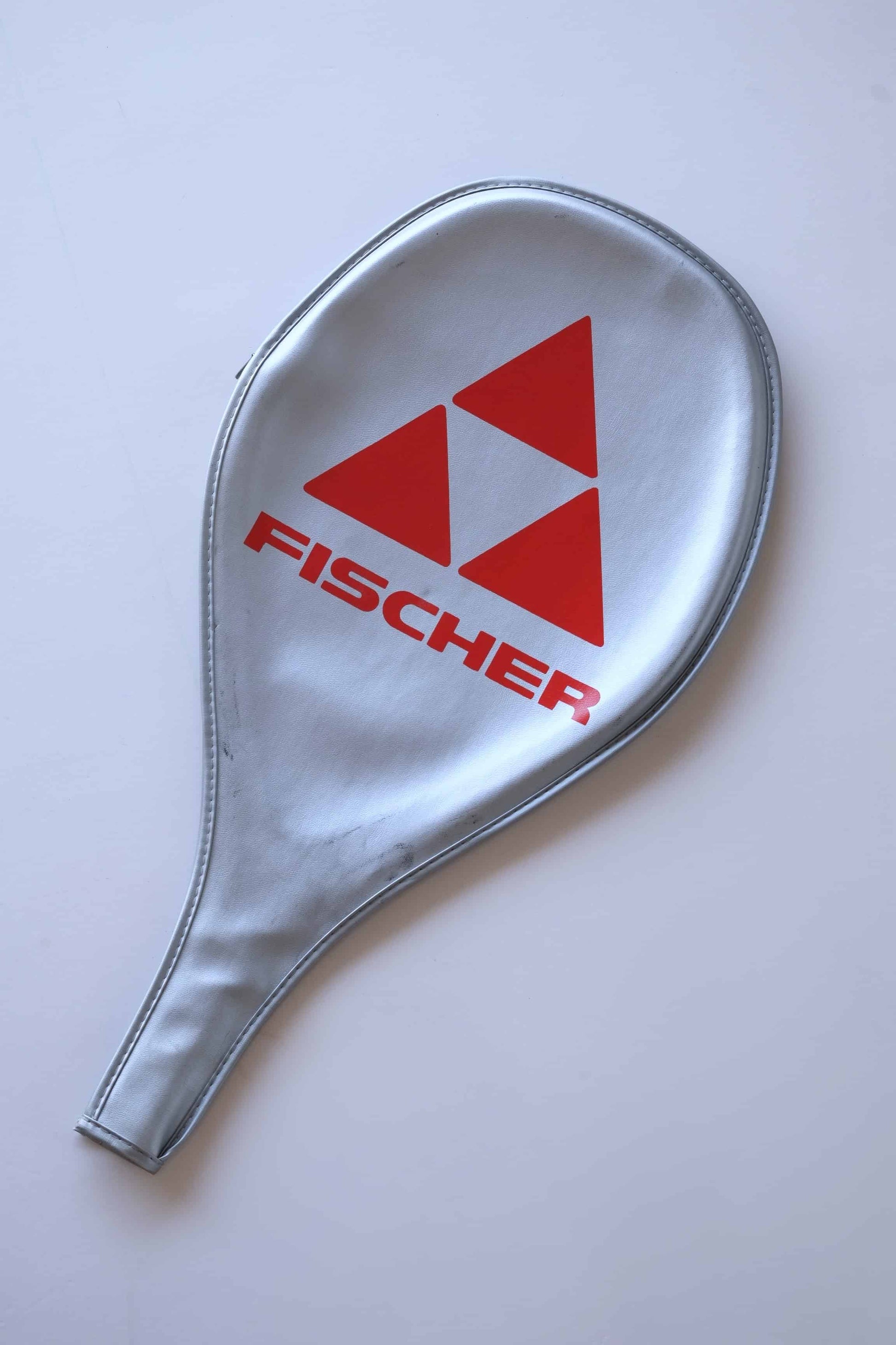 A silver tennis racket cover with a red Fischer logo.
 The logo features three interlocking triangles.