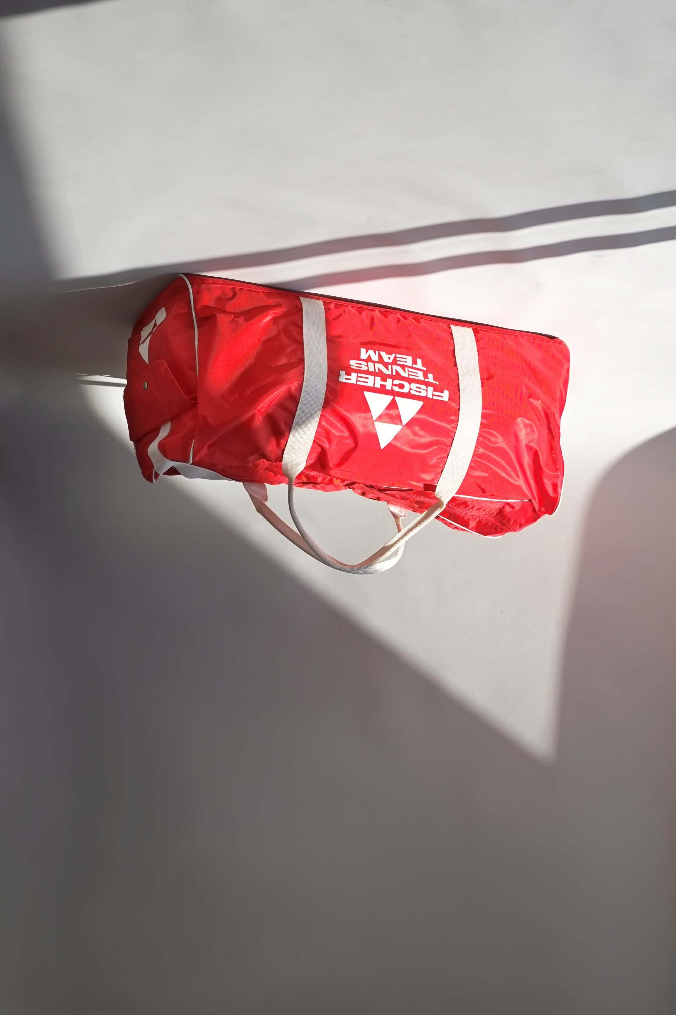 Full view of a vintage red Fischer Tennis Team sports duffle bag featuring white logo and bold text.