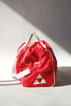 Side profile view of a vintage red Fischer Tennis Team sports duffle bag featuring white logo and bold text.
