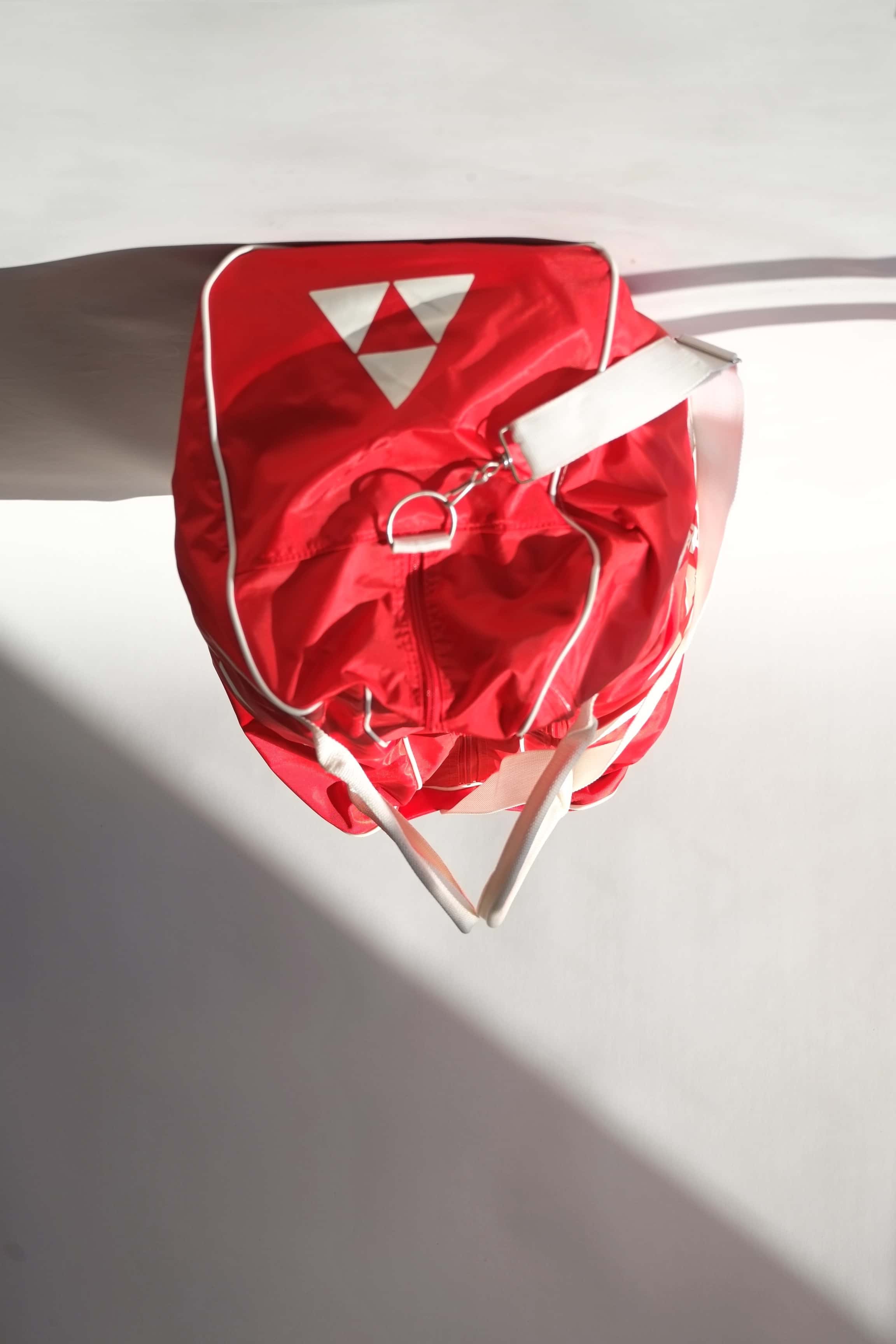 Side profile view of a vintage red Fischer Tennis Team sports duffle bag featuring white logo and bold text.