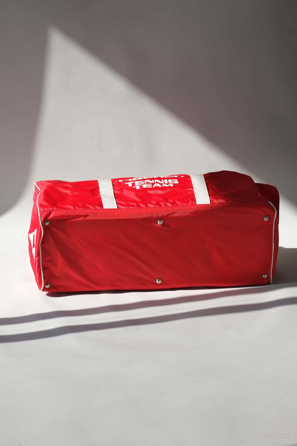Base view of a vintage red Fischer Tennis Team sports duffle bag featuring white logo and bold text.