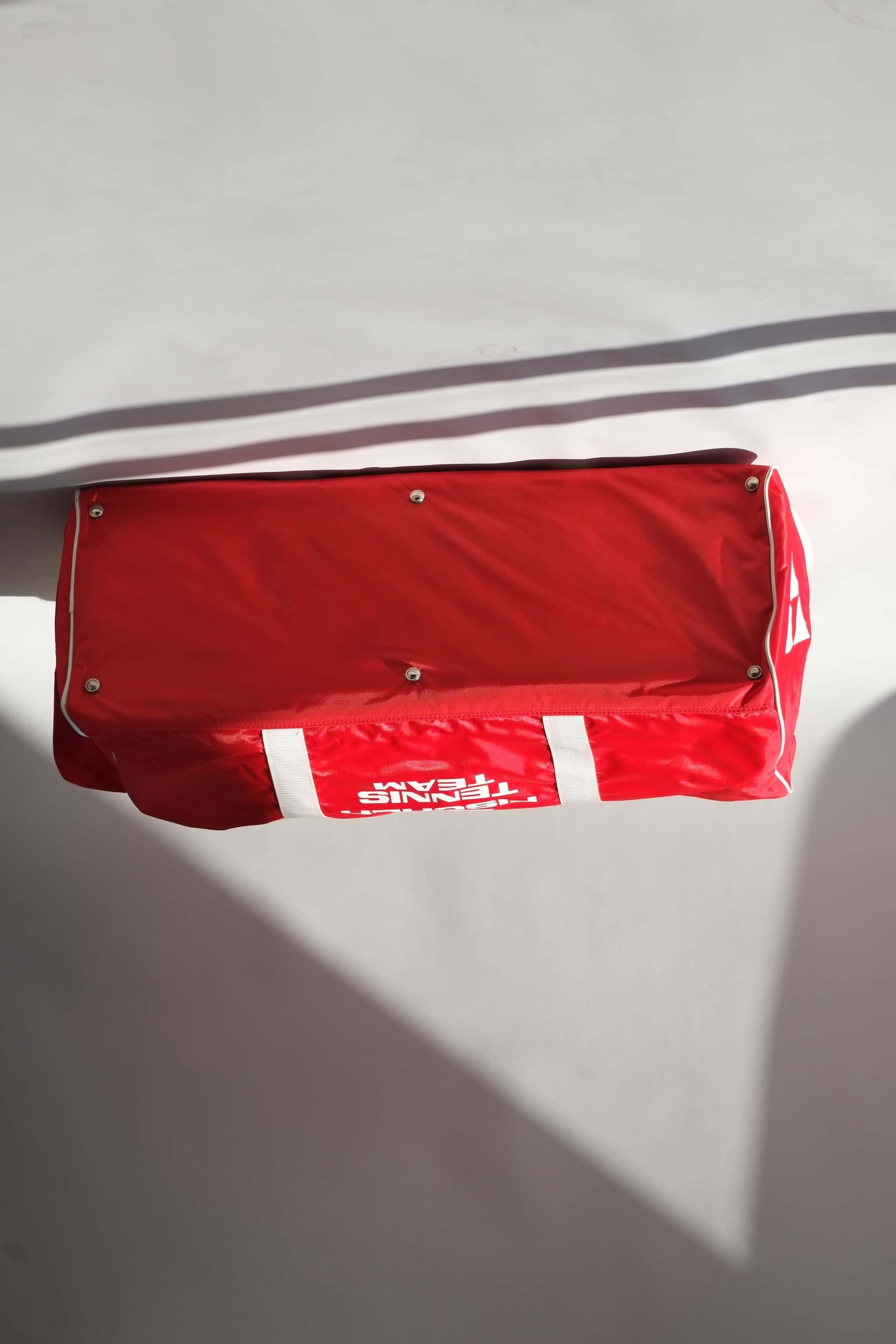Base view of a vintage red Fischer Tennis Team sports duffle bag featuring white logo and bold text.
