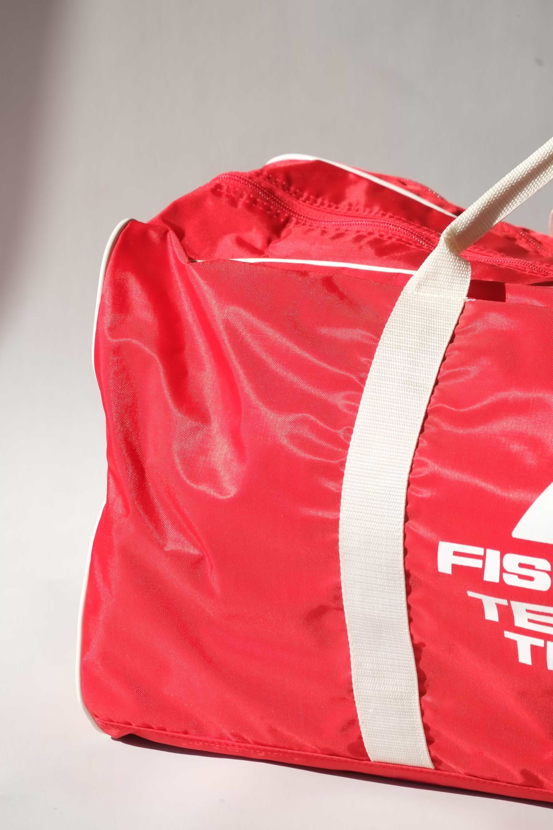 Detailed macro shot  of a vintage red Fischer Tennis Team sports duffle bag featuring white logo and bold text.