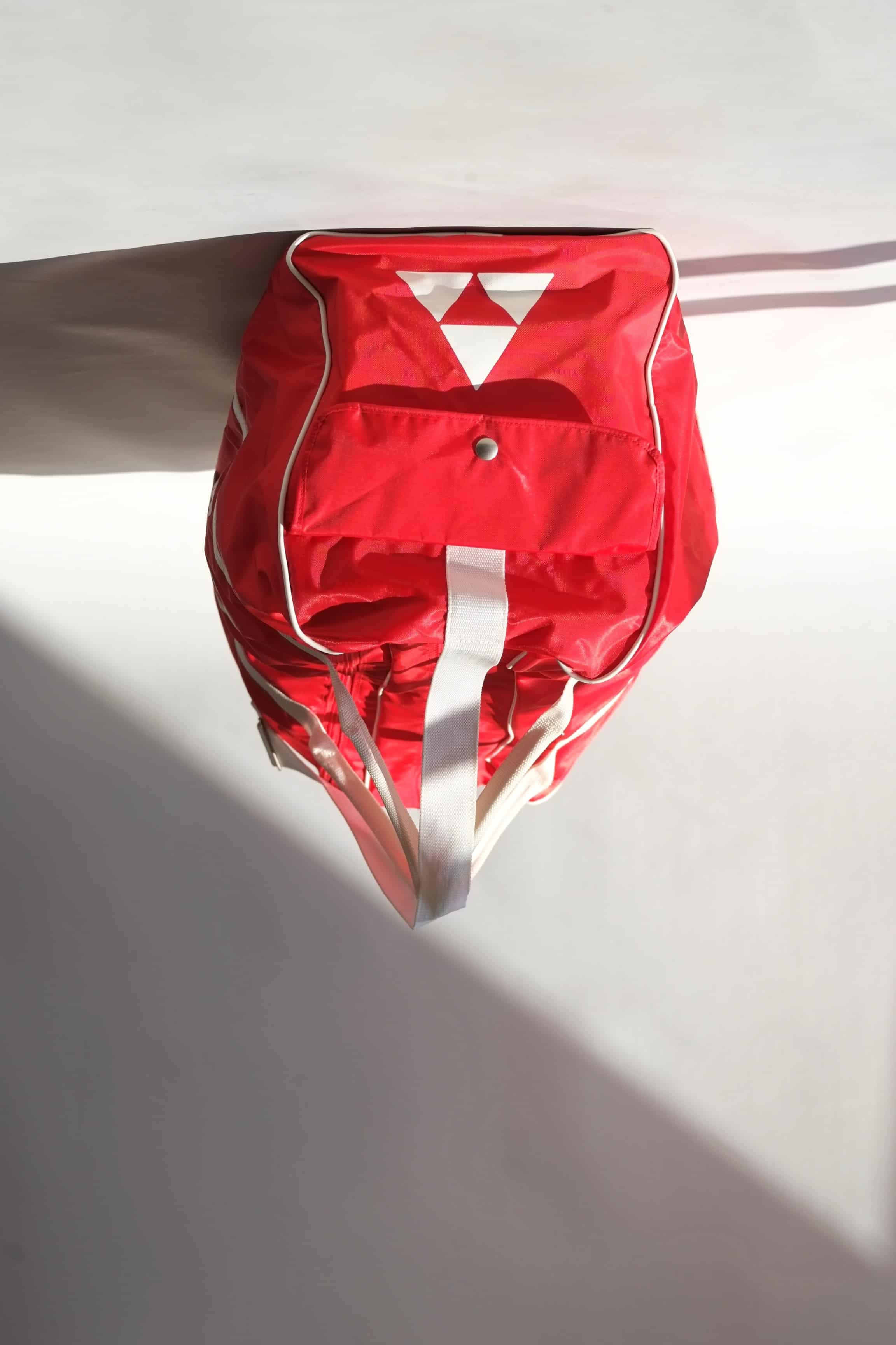 end pocket view of a vintage red Fischer Tennis Team sports duffle bag featuring white logo and bold text.