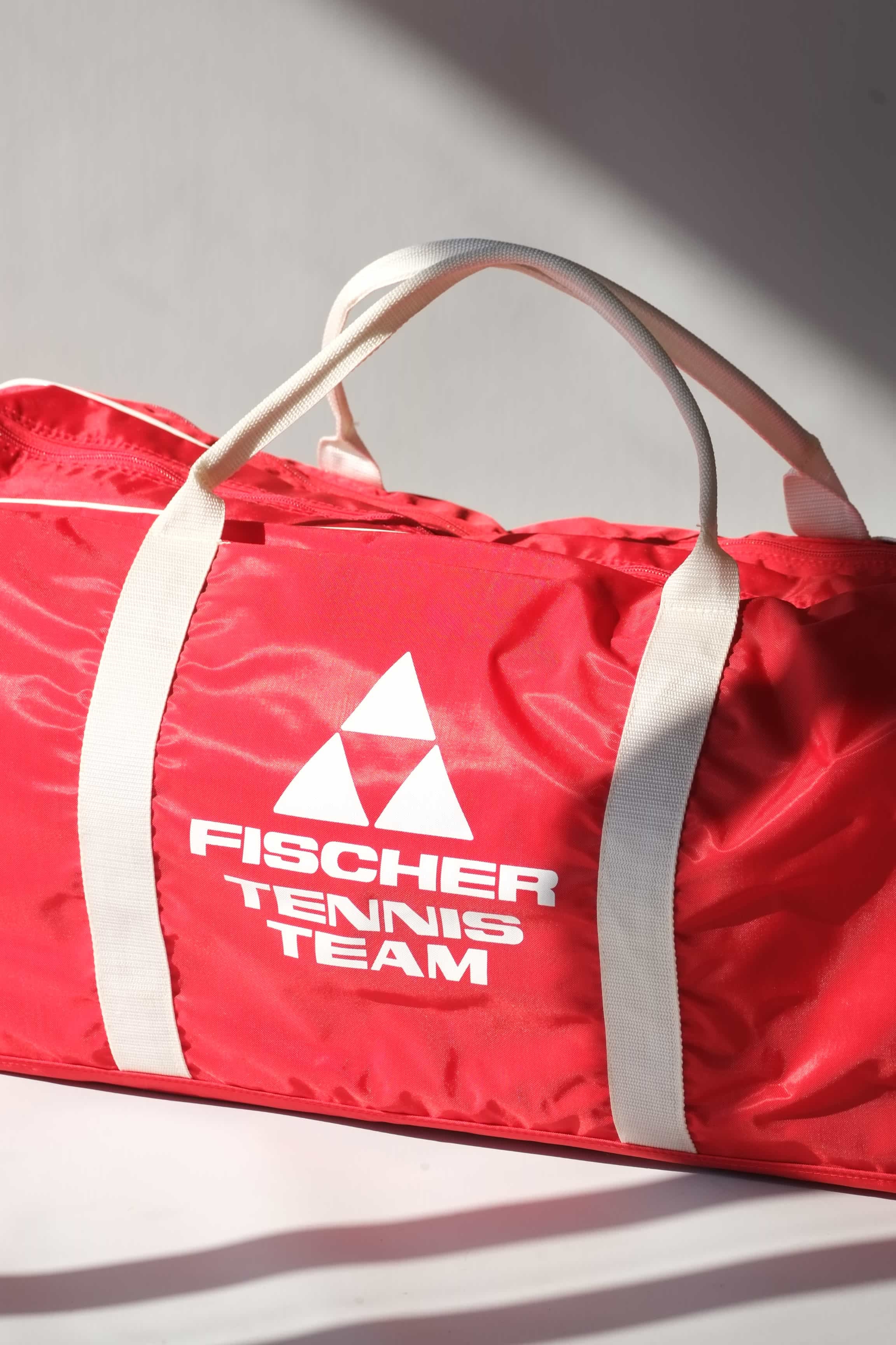 Tight shot of a vintage red Fischer Tennis Team sports duffle bag featuring white logo and bold text.