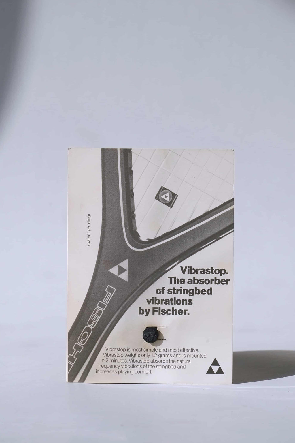 Deadstock vintage Fischer Vibrastop tennis stringbed vibration dampener, displayed on its original retail card featuring retro branding.