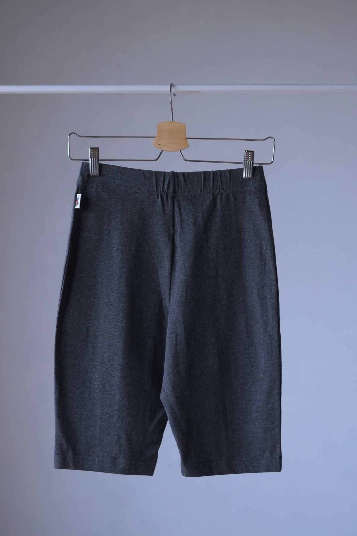 Back shot of a pair of Heather charcoal Fruit of the loom  Ladies Wear biker shorts hanging on a hanger. The shorts have an elastic waistband and are made of a soft, stretchy fabric.