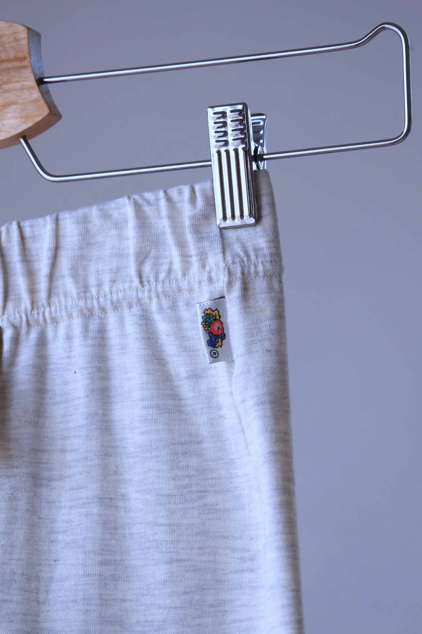 Close-up of heather beige Ladies Wear biker shorts hanging on a wooden hanger. The waistband of the shorts is visible, with the tag showing a label with a small fruit illustration.