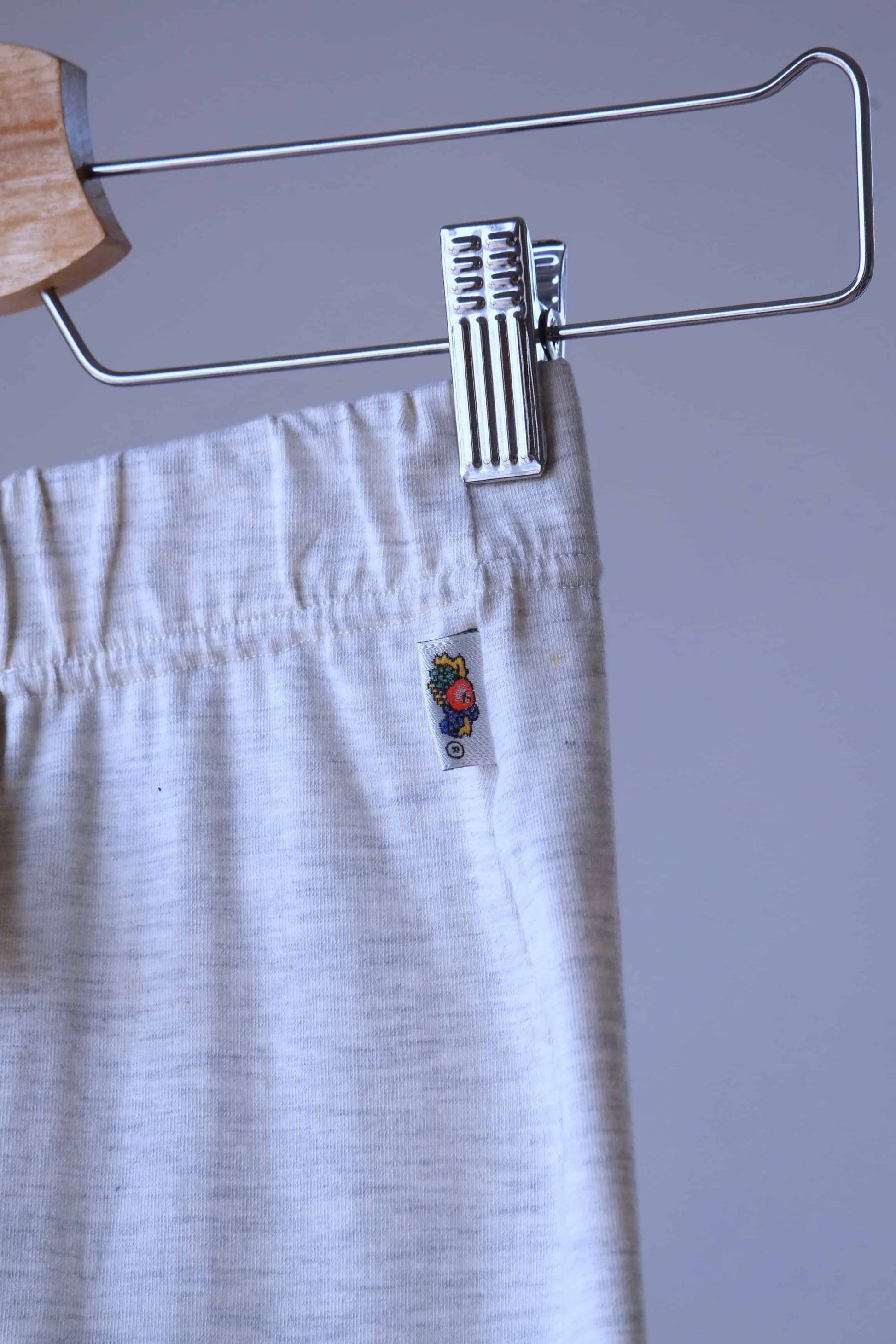Close-up of heather beige Ladies Wear biker shorts hanging on a wooden hanger. The waistband of the shorts is visible, with the tag showing a label with a small fruit illustration.