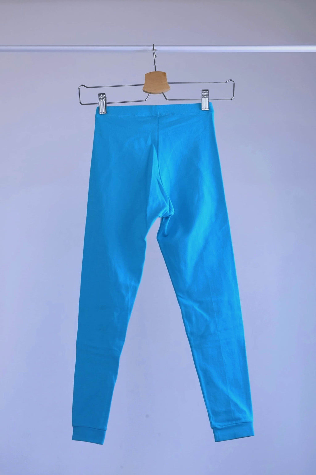 Back view of A pair of blue, vintage 90s GILDA MARX cropped leggings hanging on a metal hanger against a light gray background.