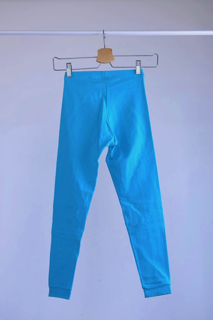 Back view of A pair of blue, vintage 90s GILDA MARX cropped leggings hanging on a metal hanger against a light gray background.