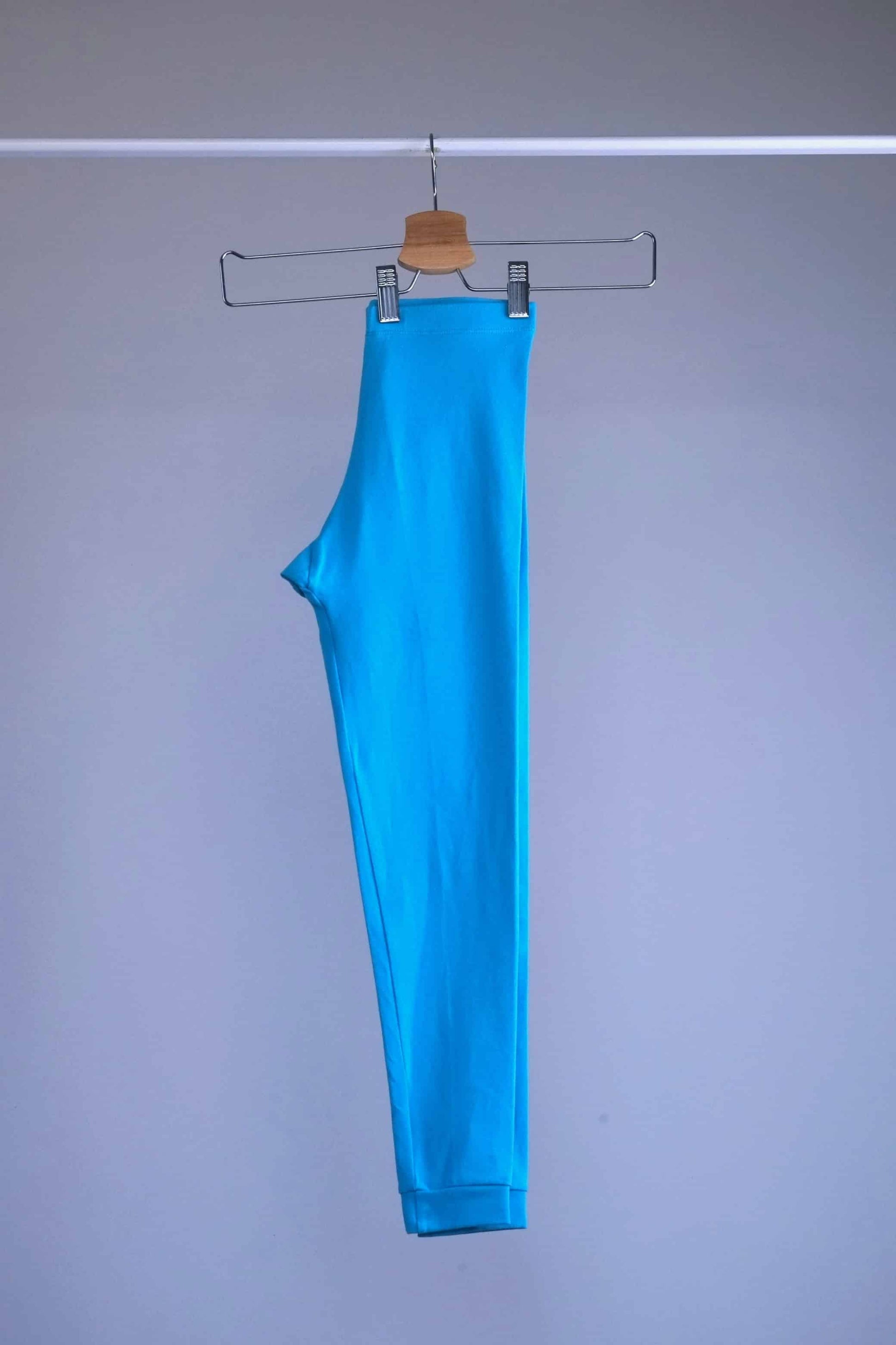 Side view of A pair of blue, vintage 90s GILDA MARX cropped leggings hanging on a metal hanger against a light gray background.