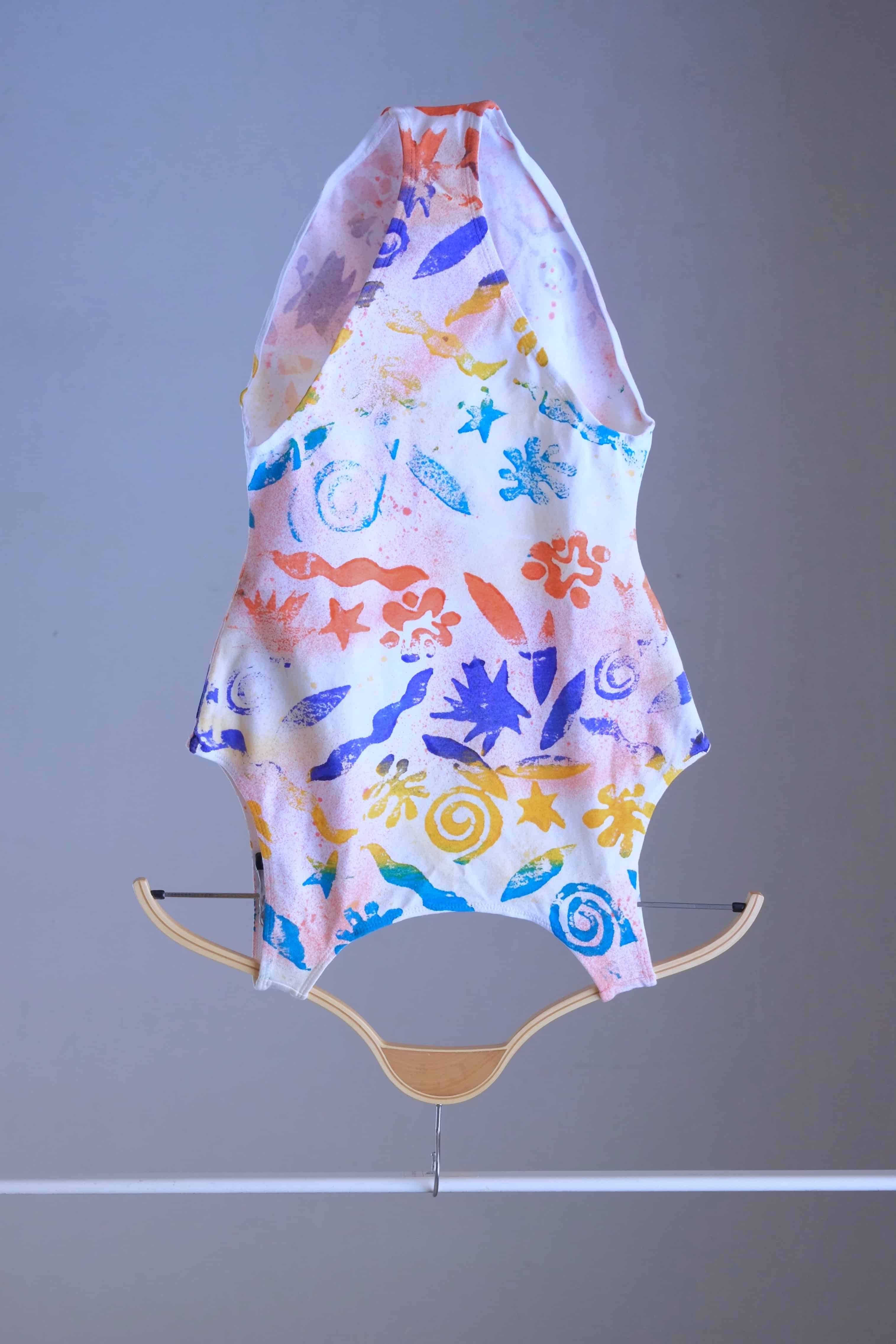 Front view of a vintage Gilda Marx leotard with an abstract beach-themed pattern on a hanger.