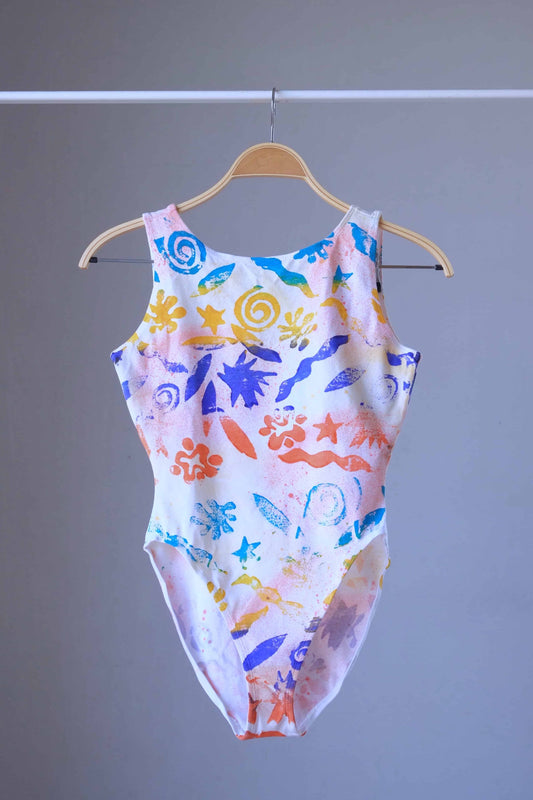 Front view of a vintage Gilda Marx leotard with an abstract beach-themed pattern on a hanger.