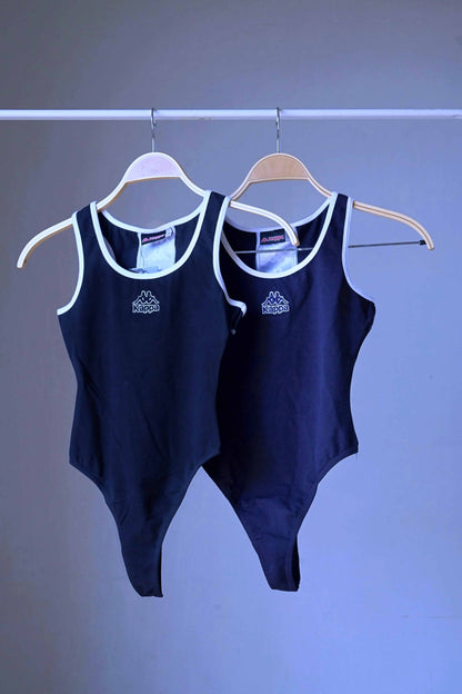 Two black KAPPA vintage 90s women's activewear leotards, one dark navy and one black, with white trim and chest logos, displayed side-by-side on hangers.