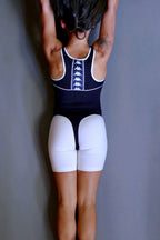 Back view of a person doing a handstand, wearing a black KAPPA vintage 90s activewear leotard with white trim and a vertical logo band, paired with white shorts, standing against a grey wall.