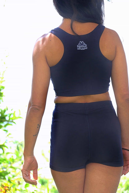 Back view of a person modeling a navy blue KAPPA vintage women's athletic crop top and shorts set outdoors. The KAPPA logo is visible on the back of the top.