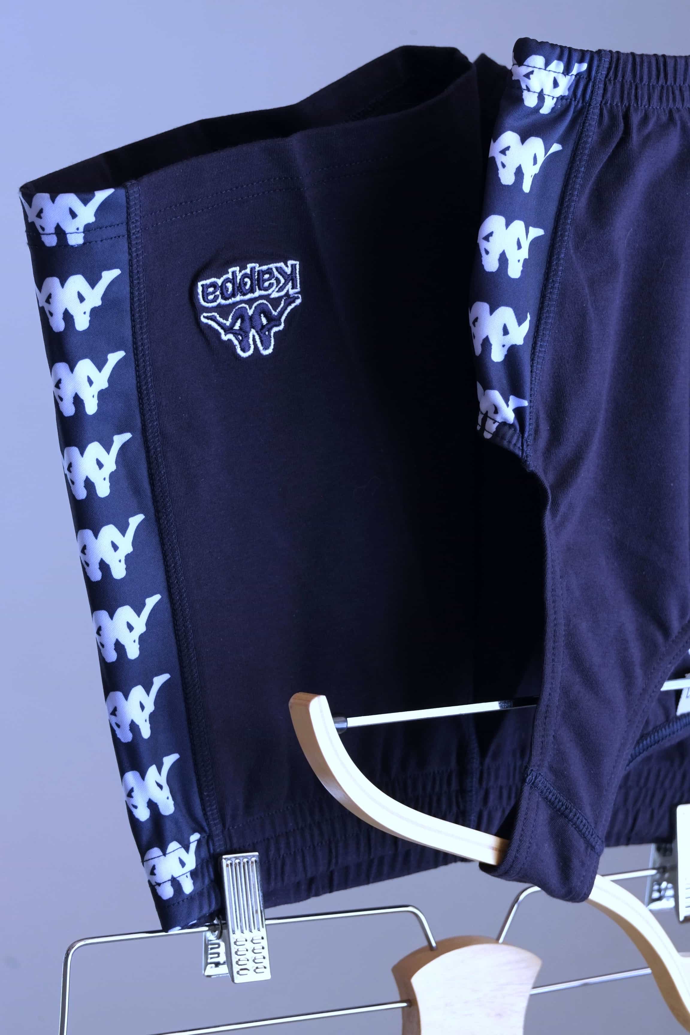 Close-up view of a navy blue KAPPA vintage women's athletic crop top and shorts set on hangers, highlighting the white KAPPA logo taping on the sides of both garments and the KAPPA logo on the shorts.