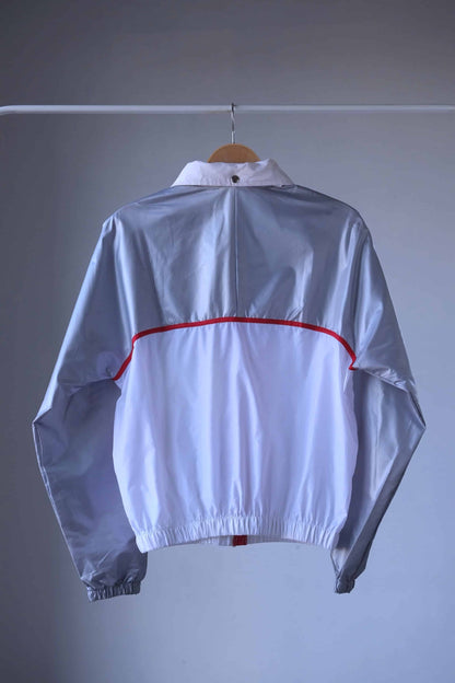 Back view of a vintage Koflach windbreaker jacket. The jacket is white with silver panels and a red stripe. It has a foldable hood and elastic cuffs.