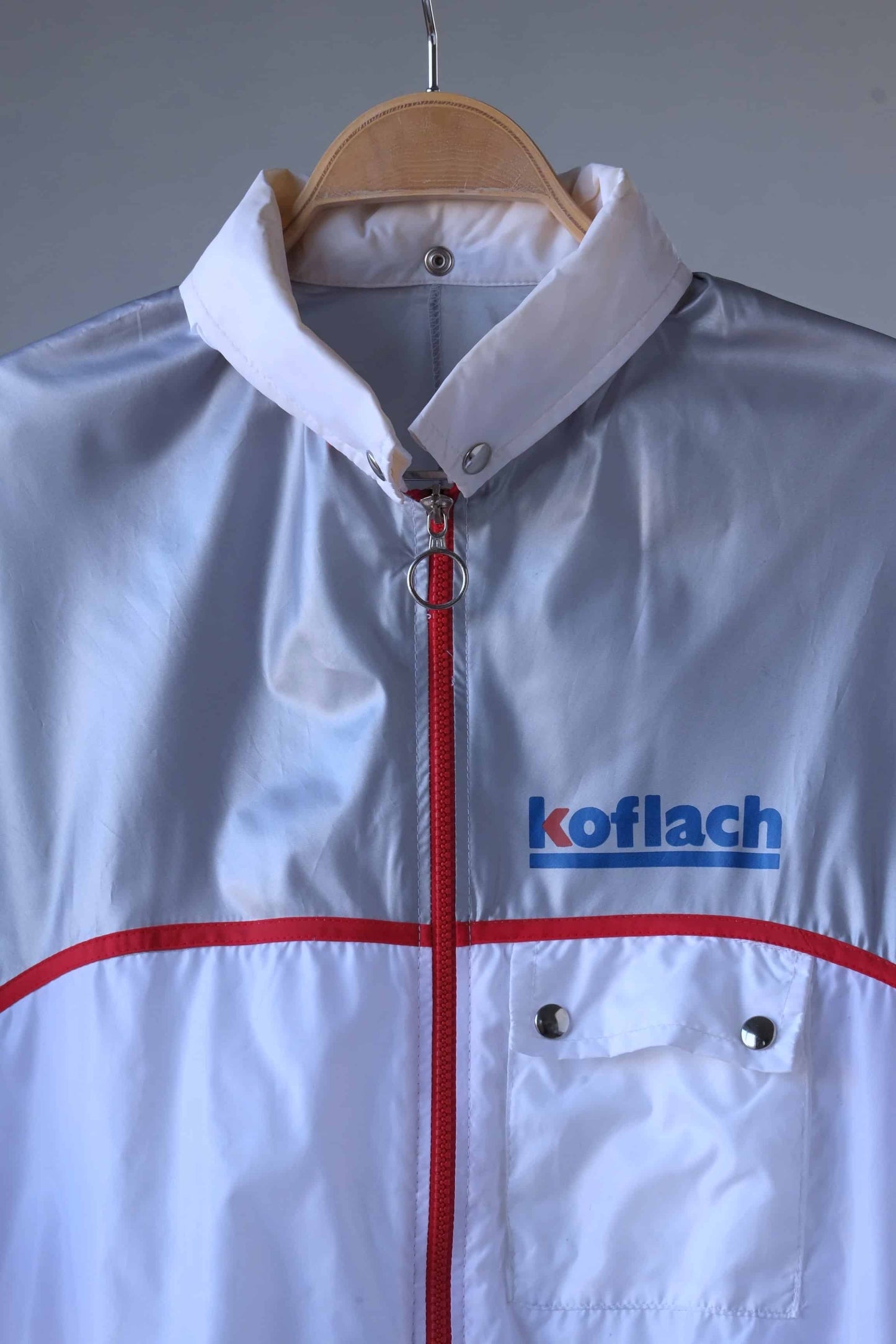 Close-up of a vintage Koflach windbreaker jacket. The jacket features a white collar, red zipper, and the Koflach logo on the chest.