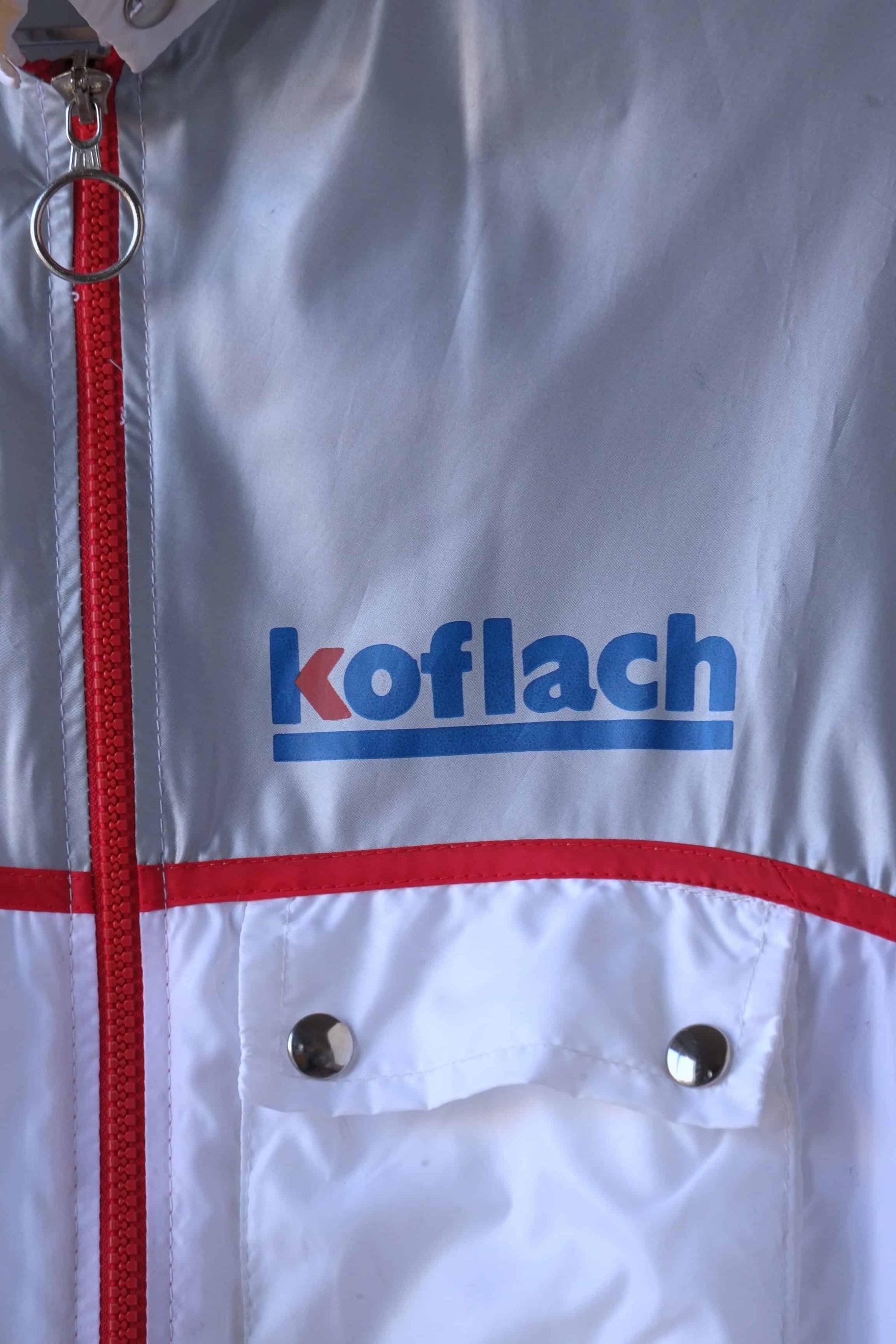 Close-up of the Koflach logo on a vintage windbreaker jacket. The jacket features a red zipper and a contrasting color block design.