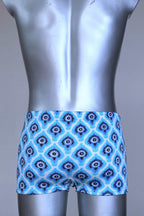 Back view of vintage 60s Lahco swim trunks in icy blue with a repeating dark blue and white geometric medallion pattern, featuring a zip pocket and brand tag.