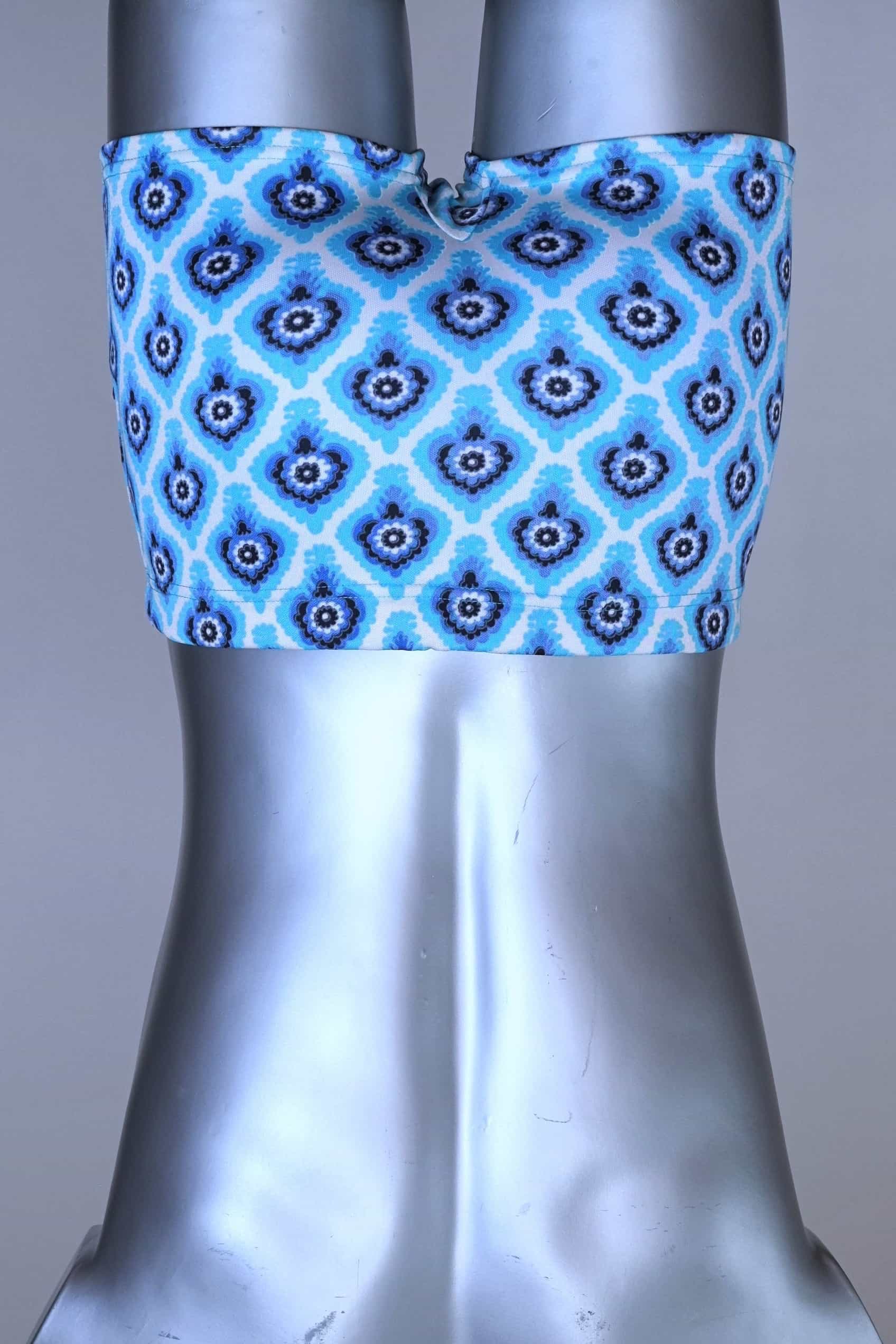 Back view of vintage 60s Lahco swim trunks in icy blue with a repeating dark blue and white geometric medallion pattern, featuring a zip pocket and brand tag.